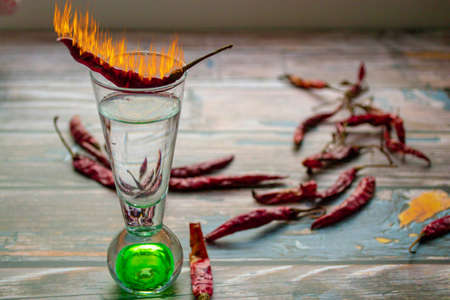 a wooden background a glass of vodka  which there is a burning pepper