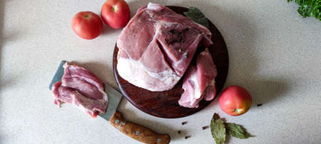 On a light background, raw fresh meat lies on a wooden board, with tomatoes and spices in it