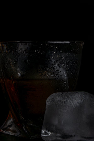 A glass of whiskey with ice cubes on a black background. Close-up.
