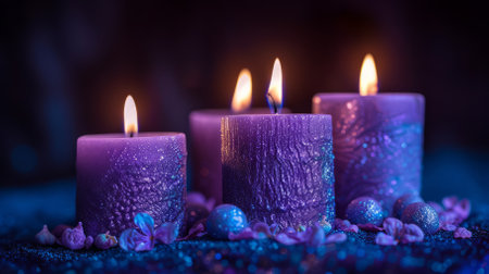 Four purple candles are burning with small purple and blue balls and flowers around them on a blue sparkly surface with a dark purple backgroundの素材