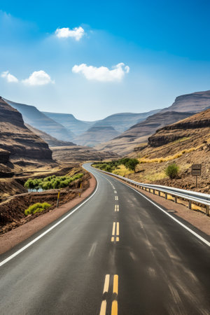 The road winds through a canyon with mountains in the backgroundの素材