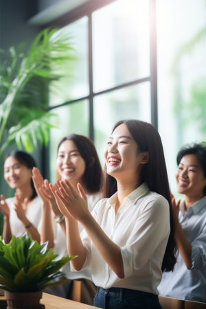 A group of four Asian businesswomen clapping and smiling in a bright officeの素材