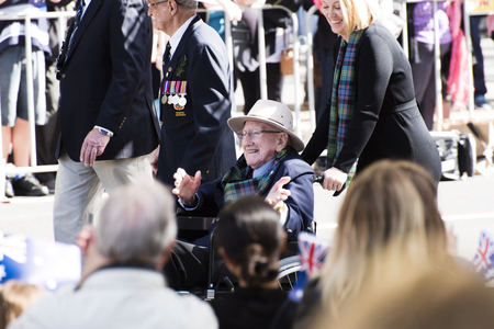 Veteran ina wheelchair smiling and waving at the crowd while being pushed by a smiling blonde woman moving down Elizabeth Stのeditorial素材
