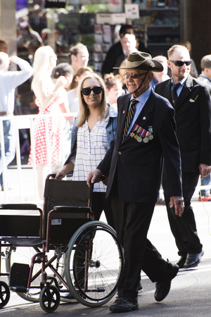 veteran wearing a slouch hat uses an empty wheelchair as support as he marches down Elizabeth St with a woman pushing the wheelchairのeditorial素材
