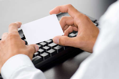 hand with white card in front of a computer keyboardの写真素材