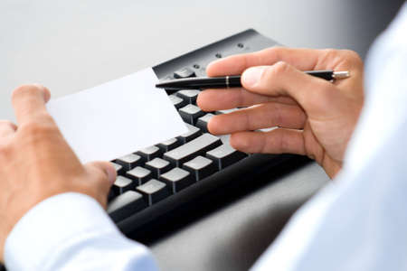 hand with white card in front of a computer keyboardの写真素材