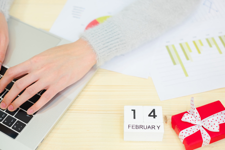 Business woman still working in Valentine day festival. using notebook laptop with new project. wooden calendar 14 February ,diagrams, Red gift box white ribbon on office desk.Hard work concept.の写真素材