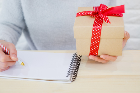 Business woman still working in Valentine day. Holding red gift box white ribbon writing notebook paper on office desk. Hard work, new year festival with copyspace.の写真素材