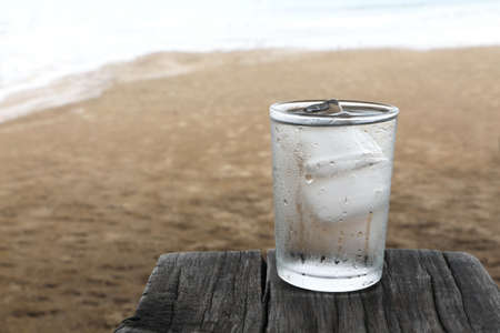 Drink water with cold ice in glass of water on old wooden plank on the beach.の写真素材