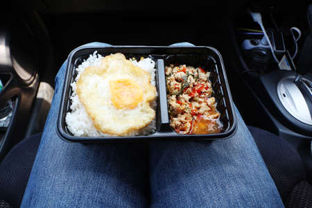 Steamed rice with fried egg and chicken basil in a plastic package placed on a woman's leg in the...