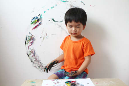 Asian boy select a colour in a paint mixing palette to paint on the concrete wall of the room. little child 3 years old painted on the concrete wall with his hands.の写真素材
