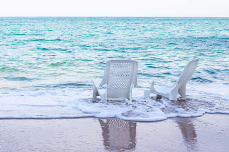 Empty white plastic chairs on the beach with beautiful white ocean waves.の写真素材