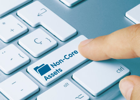 Non-Core Assets Written on Blue Key of Metallic Keyboard. Finger pressing key.