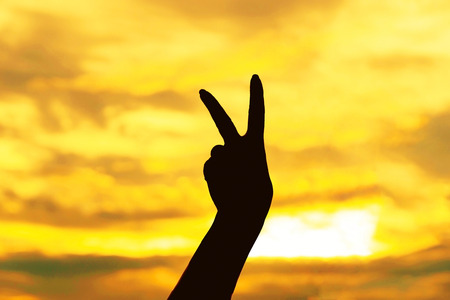 Silhouette hand with V alphabet shape gesture on sunset backgroundの写真素材