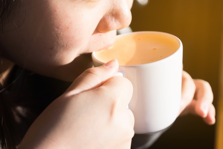 Beautiful women holding white ceramic cup and drinking milk tea inside wit sun light in the morning.の写真素材