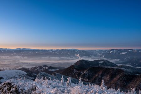 Winter landscape in mountains illuminated at sunrise with fog in valley and background Low Tatras, Slovakia Velky Chocの写真素材