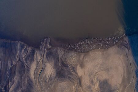 Aerial shot of a drying lake and the aftermath of it, with a large flock of herons ashore