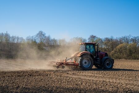 Farmer in tractor preparing land with seedbed cultivator, morning sunの写真素材