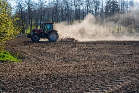Farmer plowing the field. Cultivating tractor in the field. Red farm tractor with a plow in a farm field. Tractor and Plowの写真素材