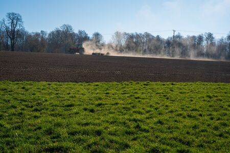 Farmer plowing the field. Cultivating tractor in the field. Red farm tractor with a plow in a farm field. Tractor and Plowの写真素材