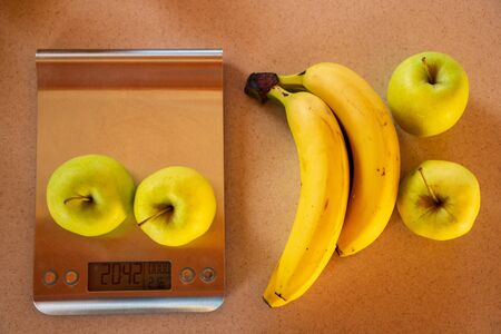 apples on a digital kitchen scale and beside are bananas and applesの写真素材