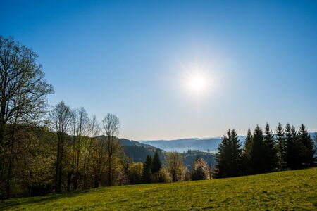 green field in the mountains with a valley below and the sun on the horizon, czechの写真素材