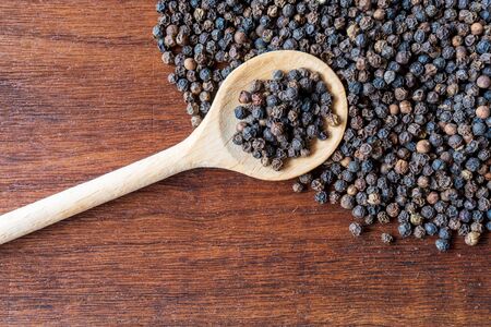 Whole black pepper balls in wooden spoon, wooden background.の写真素材
