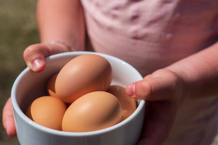 little girl holding a bowl with eggs in her hand outdoorsの写真素材