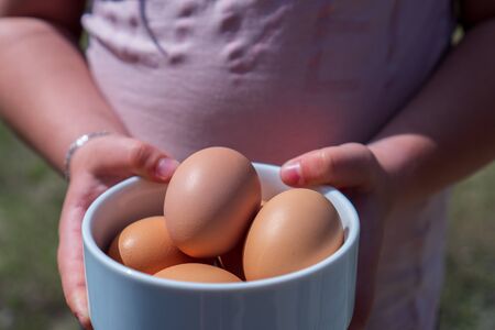 little girl holding a bowl with eggs in her hand outdoorsの写真素材