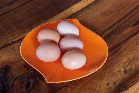 fresh brown and white chicken eggs on a orange plate on wooden background