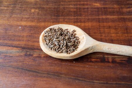 dried cumin seed or caraway in wooden spoon isolated on wooden backgroundの写真素材