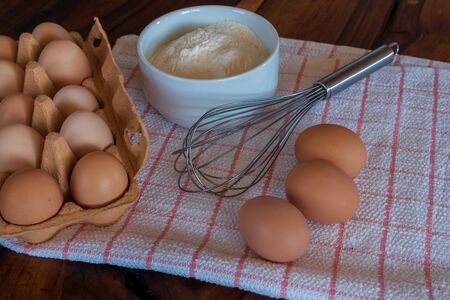 Raw chicken eggs on white bowl with flour and with whisk on wooden background. Ready to start the cooking conceptの写真素材