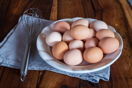 Raw chicken eggs on white plate with whisk on wooden background. Ready to start the cooking conceptの写真素材