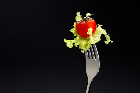 Tomato and Green Oak on a fork isolated on black background.の写真素材