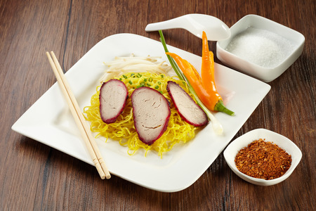 Noodle with pork on plate with wood chopstick, spoon and chilli powder, sugar in bowl on wood backgroundの写真素材