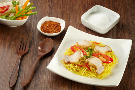 Noodle with pork on plate with wood chopstick, spoon, fork and chilli powder, sugar, vegetable in bowl on wood backgroundの写真素材