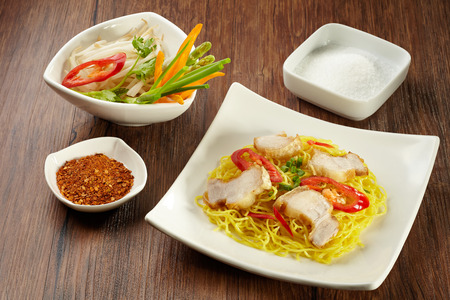 Noodle with pork on plate with wood chopstick, spoon and chilli powder, sugar, vegetable in bowl on wood backgroundの写真素材