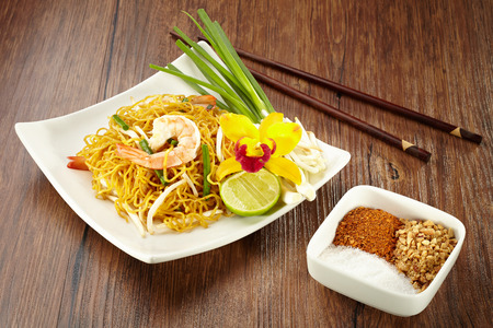 Noodle with shrimp on plate with wood chopstick  and chilli powder, peanut, sugar in bowl on wood backgroundの写真素材