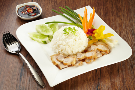 Crispy roasted belly pork with rice and sauce, stainless fork and spoon on wood backgroundの写真素材