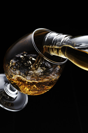 Whisky pouring in glass isolated on black backgroundの写真素材