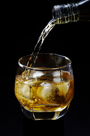 Whisky pouring on ice in glass isolated on black backgroundの写真素材
