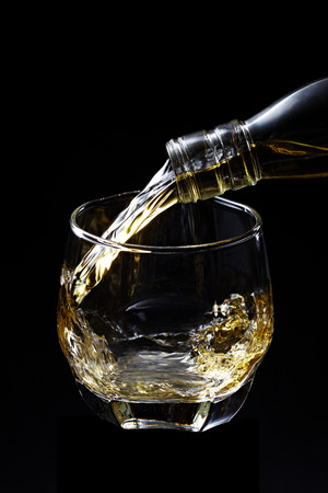 Whisky pouring in glass isolated on black backgroundの写真素材