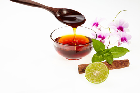 Honey in glass bowl with lime, sweet basil, cinnamon, orchid and wood spoon isolated on white backgroundの写真素材