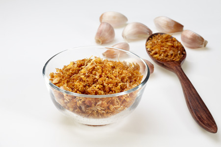 Fried garlic in glass bowl and wood spoon and garlic isolated on white backgroundの写真素材
