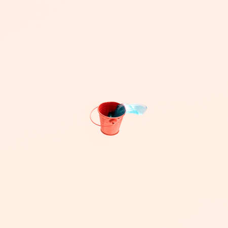 Red metal bucket and blue transparent liquid against pastel pink background. Minimal concept. Water, gardening, sustainability.の写真素材