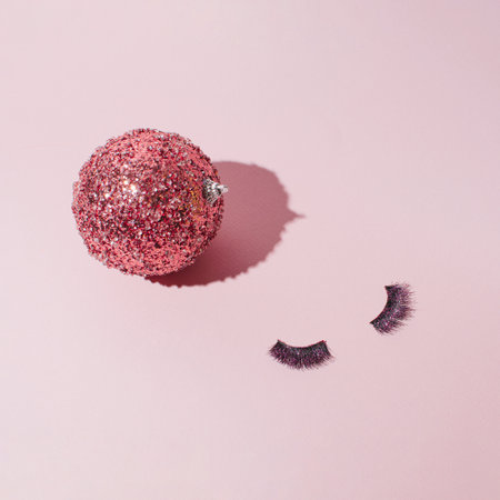 Shinny Christmas bauble and pair of false eyelashes, creative girly style layout on a pastel pink background.の写真素材