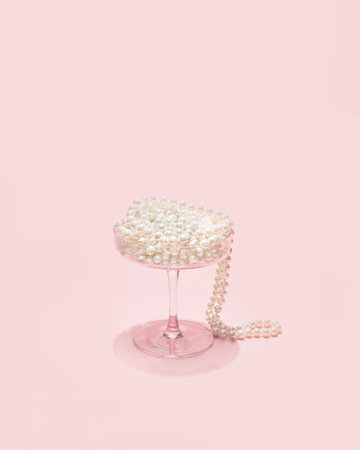 Art Deco cocktail glass with pearls, sparkling drink concept. Minimal celebration composition, pastel pink background.の写真素材