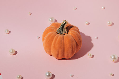 Decorative plush pumpkin and scattered pearl beads on a pastel pink background. Creative aesthetic...