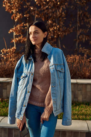 Calm and positive young female standing in a relaxed pose in the cozy alley of a quiet city square