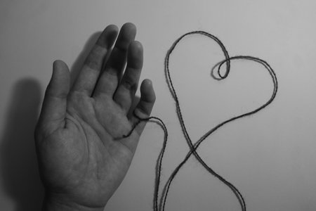 black and white image of a hand with a thread in the shape of a heartの写真素材